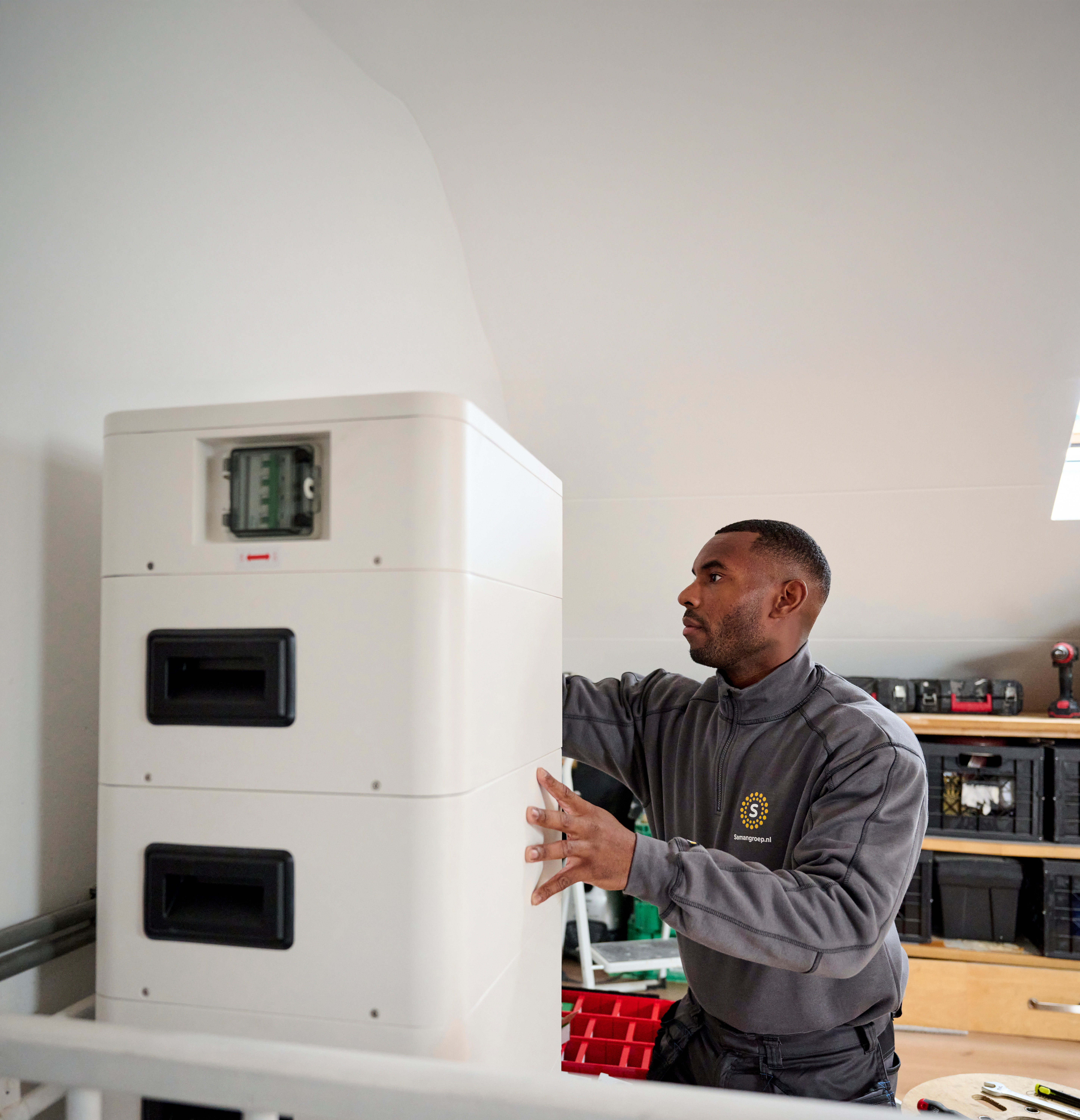 Foto van een monteur van de Saman groep die een thuisbatterij installeert zonder zonnepanelen op een zolder kamer